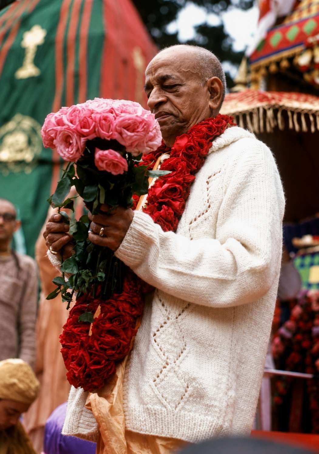 A person in traditional attire is holding a bouquet of red roses amidst decorations and other people.
AI-generated content may be incorrect.